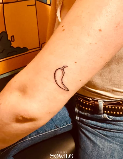 Tatouage fin représentant un piment sur le bras d'une femme