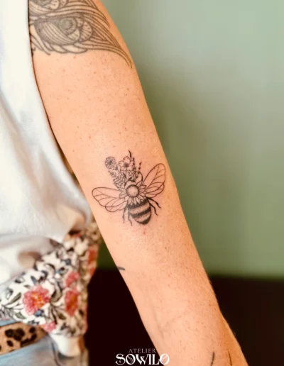 Tatouage bras, femme , représentant une abeille avec des fleurs fait par l'Atelier Sowilo