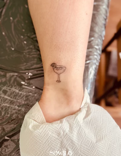Tatouage cheville femme, représentant un Cocktail de façon minimaliste en trait très fin fait par l'Atelier Sowilo